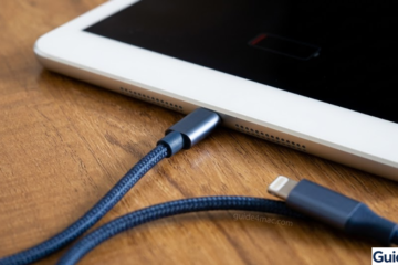 White iPad connected to a blue braided charging cable on a wooden desk, showing a low battery icon to troubleshoot a force restart.