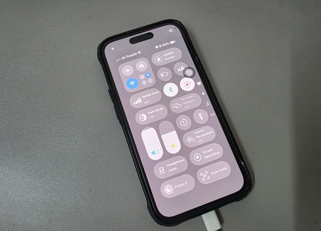iPhone connected to charger with Control Center open on screen.