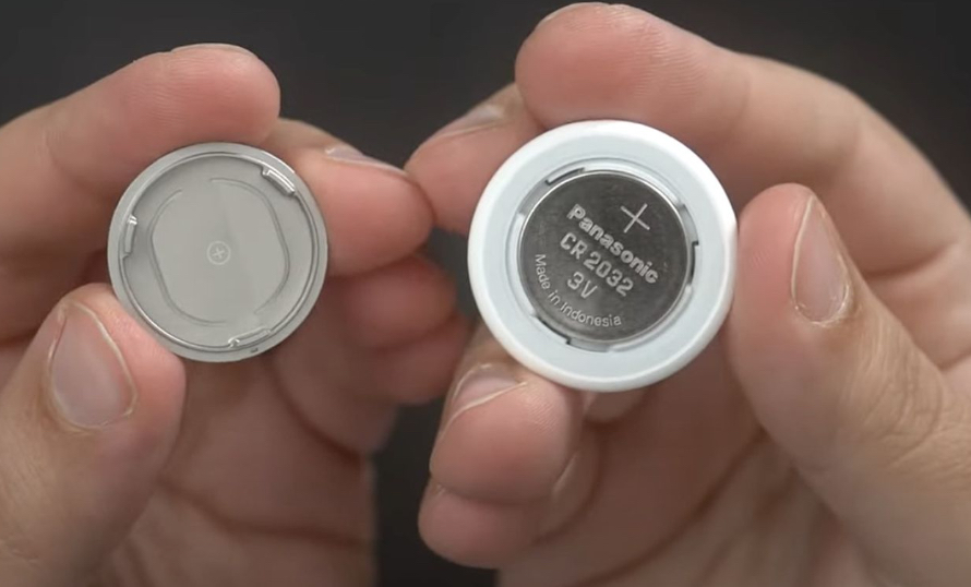 Inserting a new CR2032 battery into AirTag with positive side facing up.